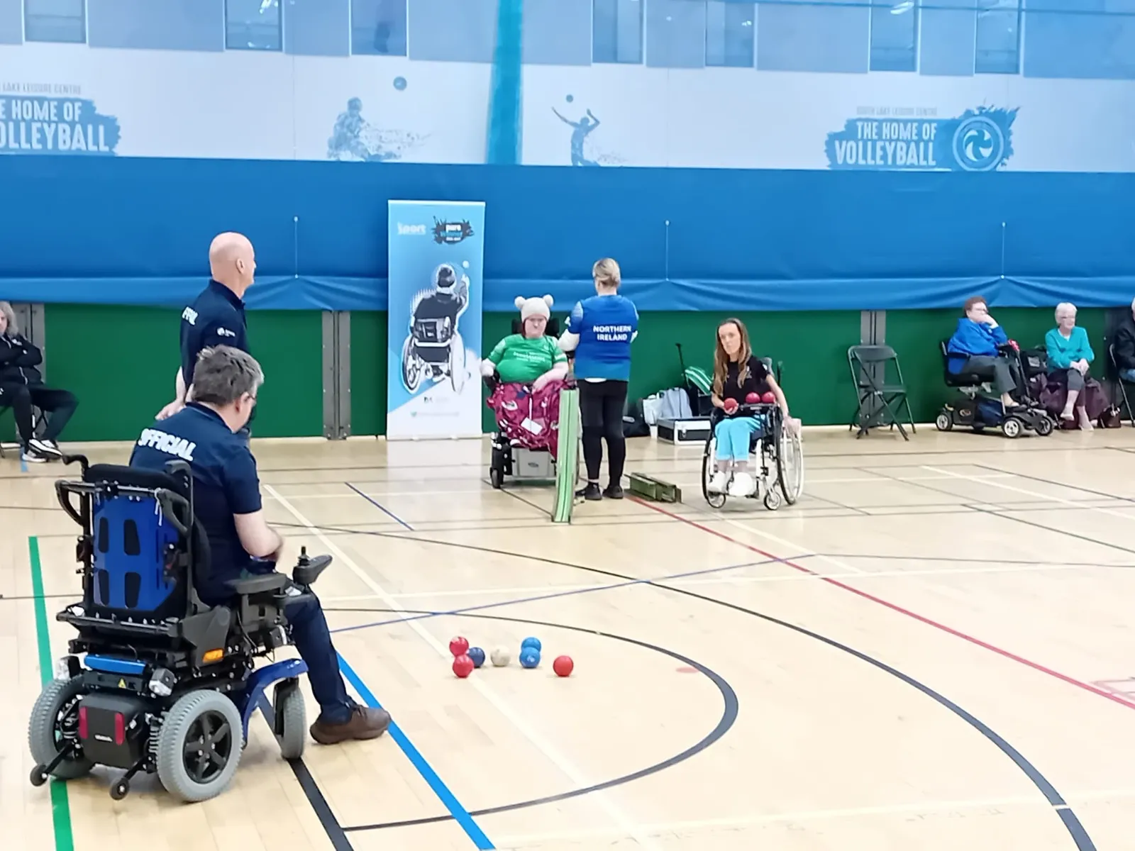Officials and players courtside at an NI Boccia League fixture, with red and blue balls grouped around the jack