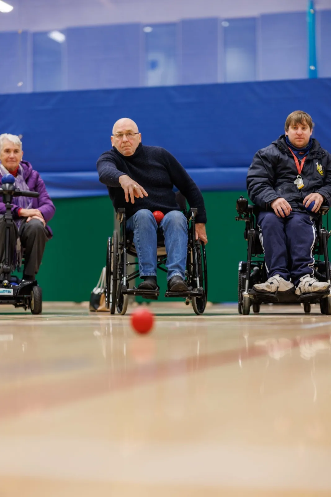 An NI boccia athlete releases a red ball down the court during a match