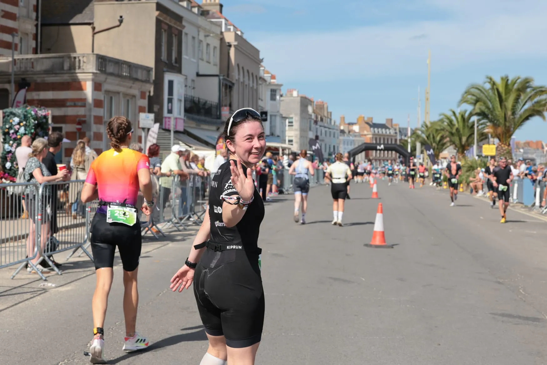 Emily Bond waving while running along the seafront at IRONMAN 70.3 Weymouth