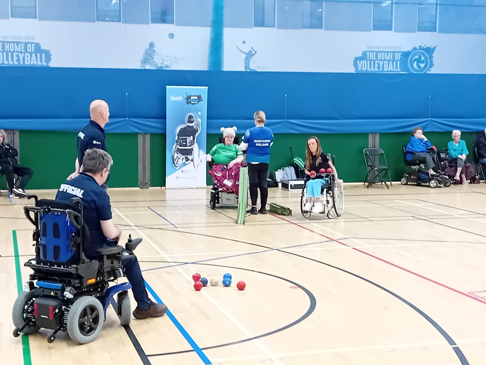 Officials and players courtside at an NI Boccia League fixture, with red and blue balls grouped around the jack
